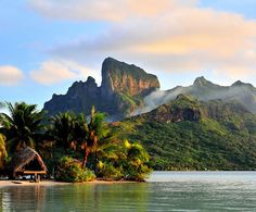 an island with palm trees and mountains in the background