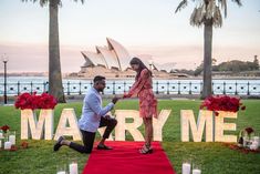 a man kneeling down next to a woman on a red carpet in front of the sydney opera