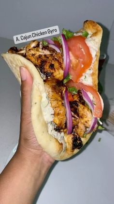 a hand holding a chicken gyro with tomatoes and onions