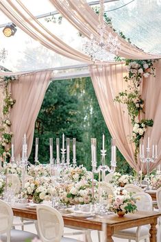 an outdoor wedding reception setup with white flowers and greenery on the table, chandeliers hanging from the ceiling