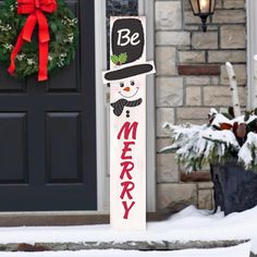 a wooden sign that says be merry in front of a door with snow on the ground