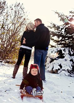 a man and woman standing next to a child on a sled