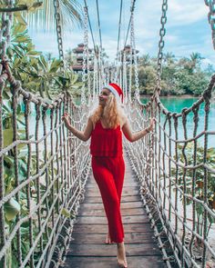 a woman in red is walking across a rope bridge