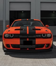 an orange and black striped dodge car parked in front of a garage door on the street