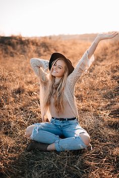 a young woman sitting on the ground with her arms in the air and smiling at the camera