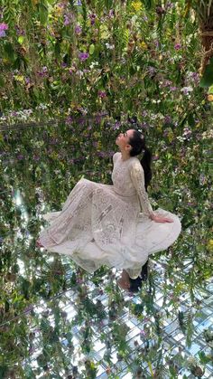 a woman in a white dress is sitting on the ground surrounded by plants and flowers