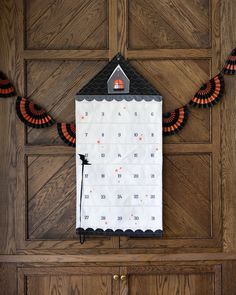 a house shaped calendar hanging on a wooden door with orange and black decorations around it