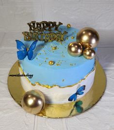 a blue birthday cake with gold decorations and butterflies on it's top, sitting on a white tablecloth