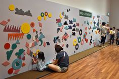 people are sitting on the floor in front of a wall covered with colorful paper cutouts