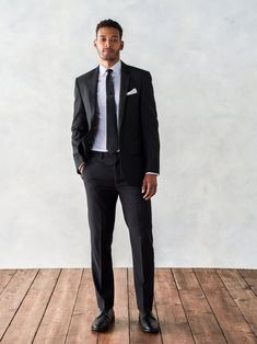 a man in a suit and tie standing on a wooden floor with his hands in his pockets