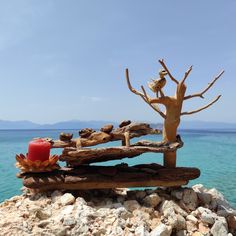 a wooden bench sitting on top of a rocky beach next to the ocean with a red candle