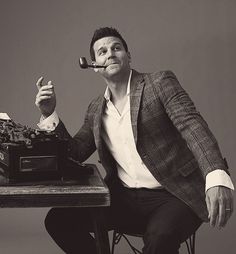 a man sitting at a table with an old typewriter and pipe in his mouth