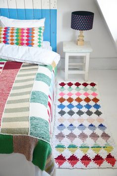 a bed with colorful bedspread and pillows on it next to a small table