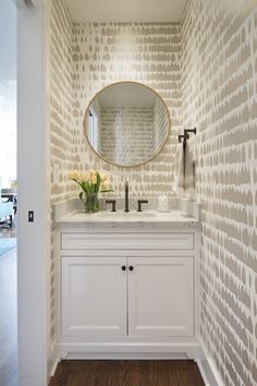 a bathroom with a sink, mirror and wallpapered walls in the background is a wood floor