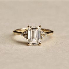 an emerald cut diamond ring with three diamonds on the band and side stones in yellow gold