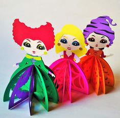 three paper dolls are standing next to each other on a white surface and one is wearing a colorful dress