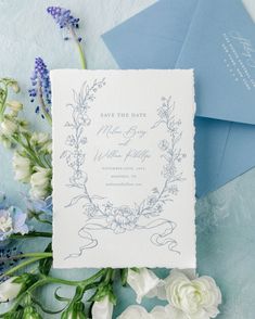 the wedding stationery is surrounded by flowers and blue envelopes