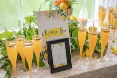 a table topped with champagne glasses filled with yellow liquid and lemons next to a sign