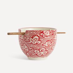 a red and white bowl with chopsticks sticking out of the side on a white background