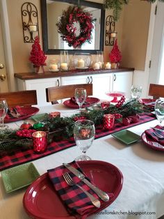 the table is set for christmas dinner with red and green place mats, plaid napkins, silverware