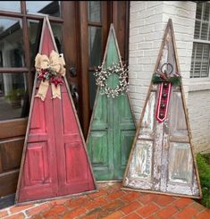 three wooden christmas trees sitting on top of a red brick floor next to a door