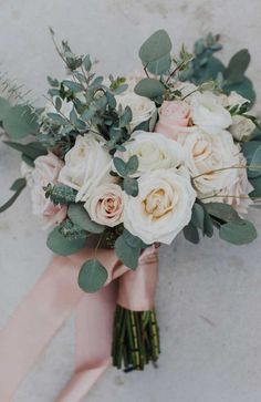 a bridal bouquet with white roses and greenery on the side of a wall