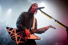 a man with long hair holding a guitar on stage