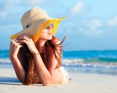 a woman laying on the beach wearing a sunhat and sunglasses with her hair blowing in the wind