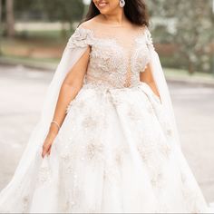 a woman in a white wedding gown and veil smiles at the camera while walking down the street