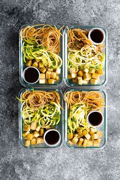 four glass containers filled with food on top of a gray table next to sauces