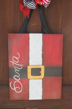 a christmas door hanger with a santa suit on it's front and red, white, and black striped ribbon