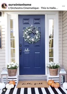 a blue front door with two pumpkins on the steps and a black and white striped rug