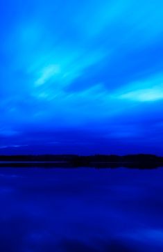 the sky is blue and there are clouds in the sky above water with trees on either side