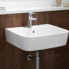 a white bathroom sink sitting on top of a wooden wall next to a shelf with vases