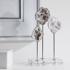 three crystal sculptures sitting on top of a white counter next to a framed painting and mirror