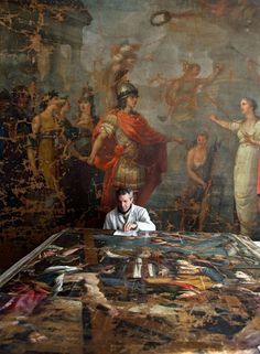 a man sitting at a table in front of a painting with other people around it