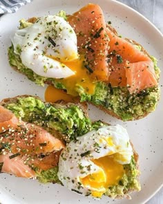 two pieces of toast with eggs, avocado and salmon on them sitting on a white plate