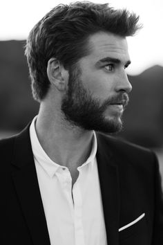 a black and white photo of a man with a beard in a suit jacket looking off to the side