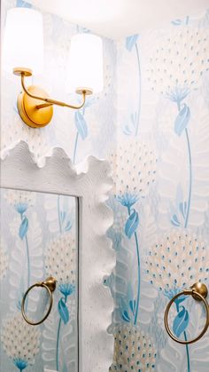 a bathroom with blue and white wallpaper, gold fixtures and two lights on the mirror