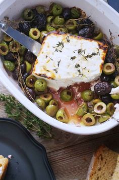 a bowl filled with olives and feta cheese next to bread on a table