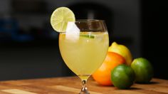 a close up of a wine glass on a table with citrus and limes in the background