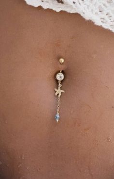 the back of a woman's stomach with a gold chain and dangling belly ring