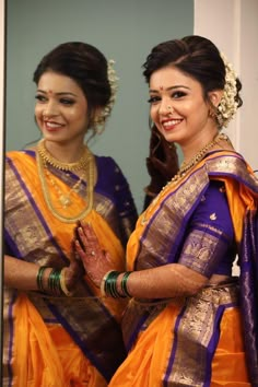 two women dressed in yellow and purple sari are posing for the camera with their hands together