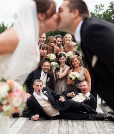 a bride and groom kissing on the ground with their wedding party in the backgroud