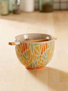 an orange and green bowl with wooden spoons in it