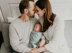 a man and woman sitting on a couch holding a baby in their arms while they are kissing each other