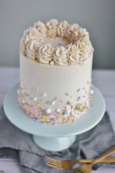 a white cake with sprinkles and frosting on a plate next to a fork