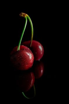 two cherries with water droplets on them are shown against a black background in this still life photograph