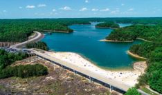 an aerial view of a bridge over a body of water surrounded by trees and sand