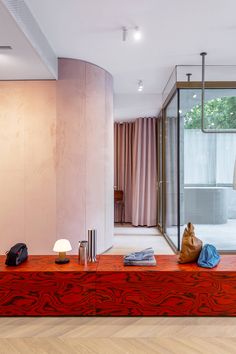 a living room with a red couch and wooden table in front of a glass wall